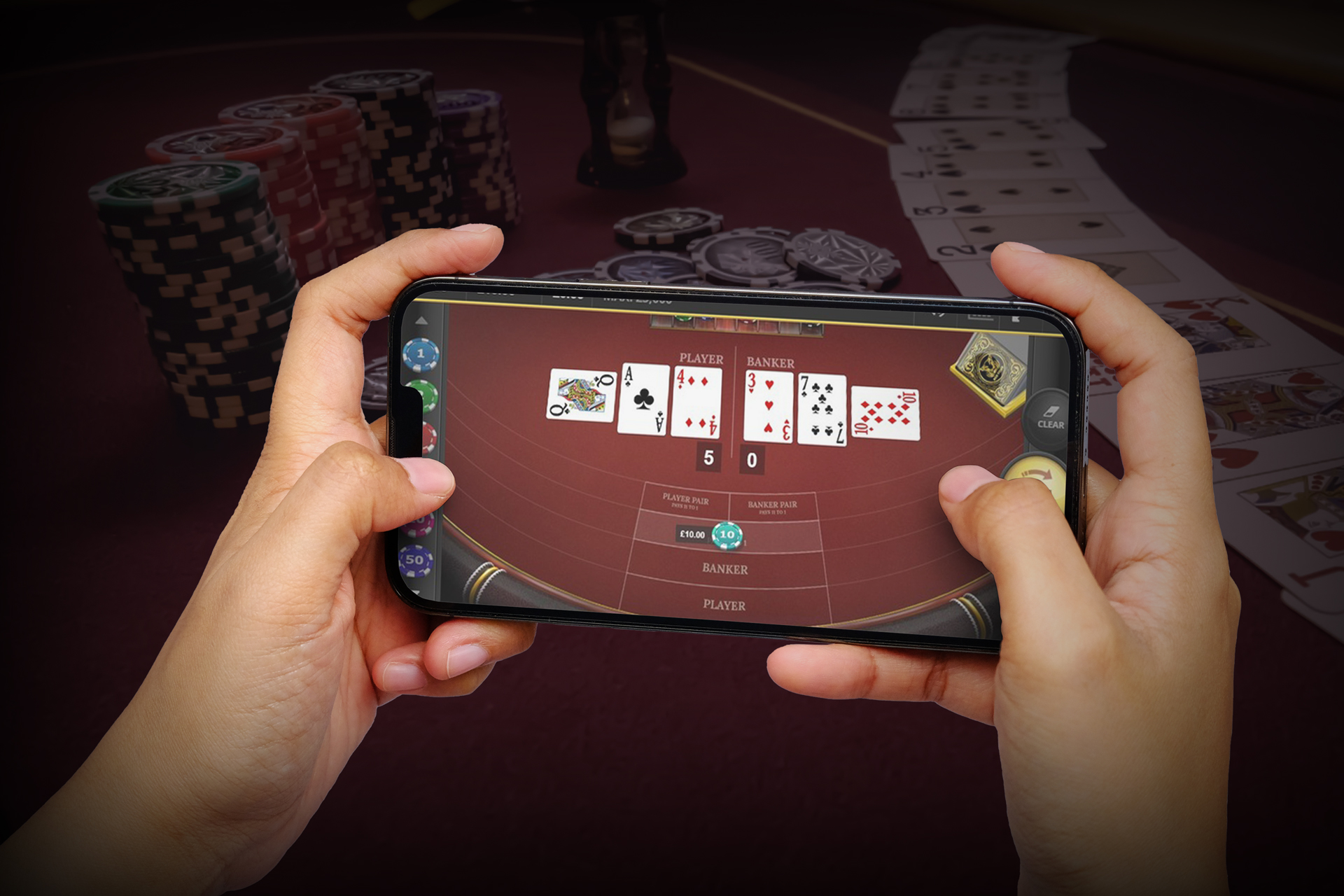 Hands holding a smartphone displaying a baccarat game, with poker chips and playing cards in the background. The image represents mobile gambling, highlighting the convenience of playing casino games at the best online baccarat casinos.